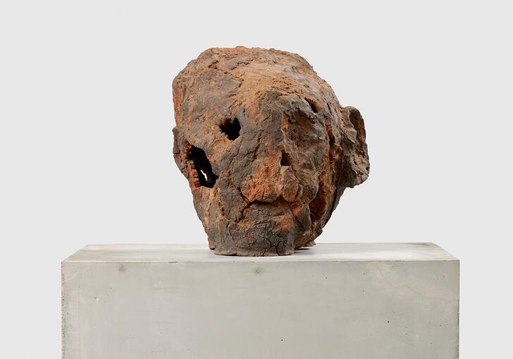 A terracotta sculpture that resembles a human head, sitting on a concrete plinth